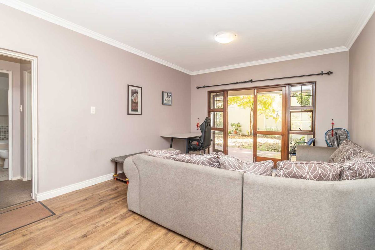 A living room featuring laminate flooring, crown molding, and wooden framed glass doors providing direct access to the outdoor area.