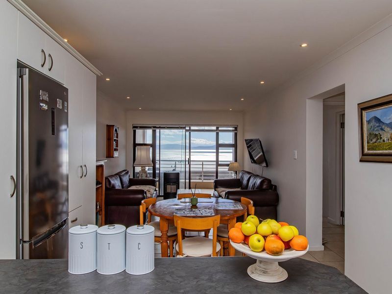 Open-plan living and kitchen area featuring modern cabinetry, recessed lighting, and large sliding doors leading to a balcony with scenic water views.