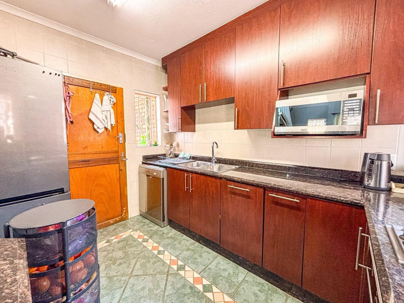 A functional kitchen featuring dark wood cabinetry, granite countertops, a built-in microwave, and tiled flooring with a decorative border.
