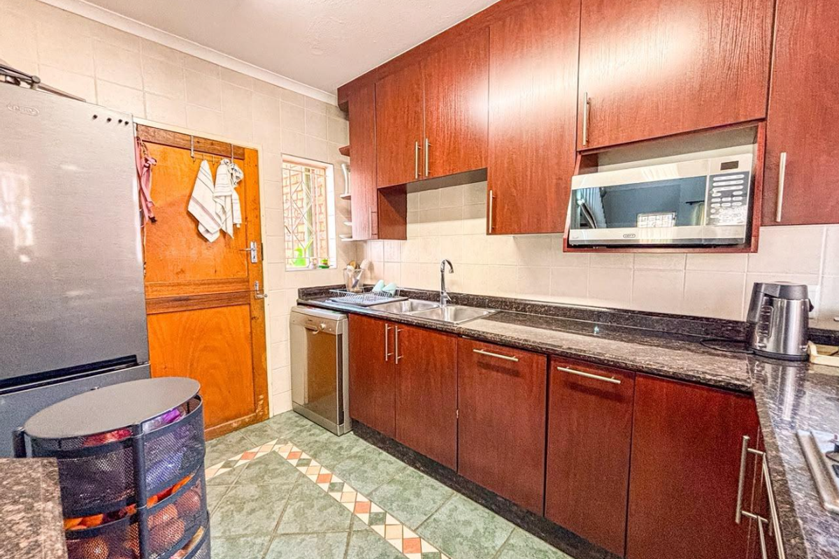 A functional kitchen featuring dark wood cabinetry, granite countertops, a built-in microwave, and tiled flooring with a decorative border.