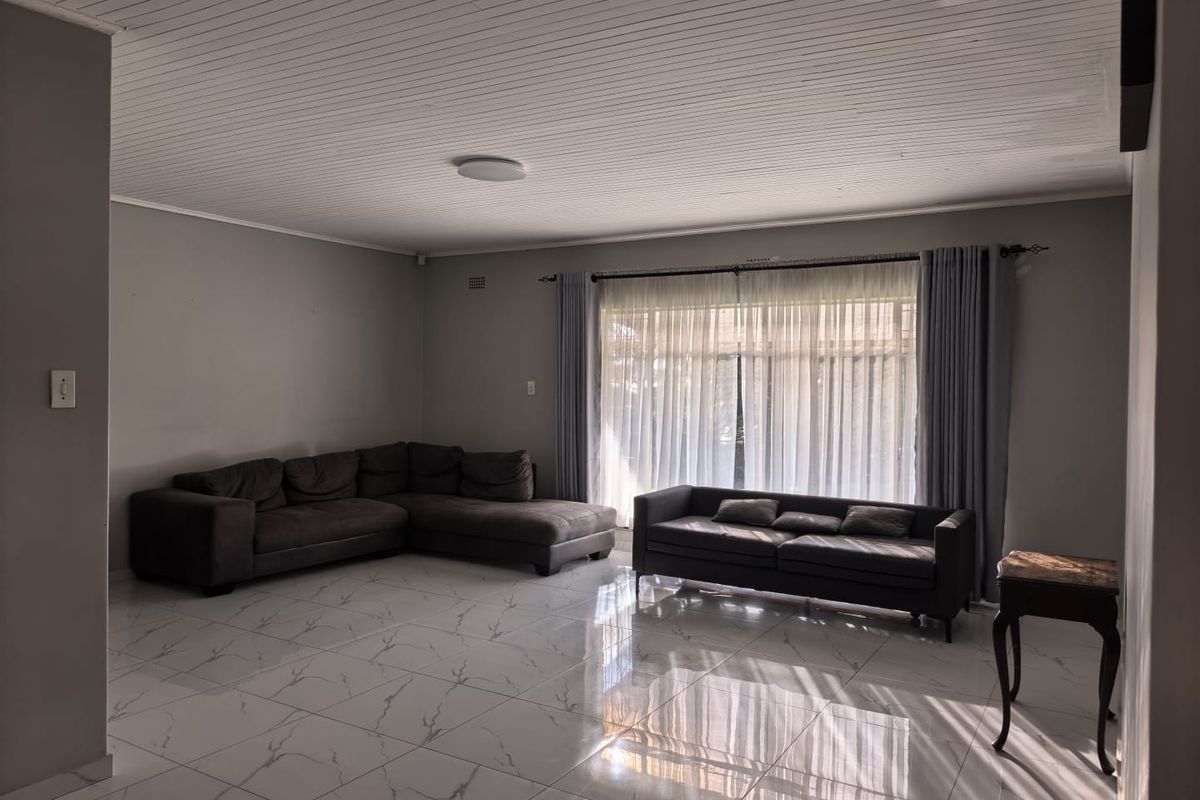 Spacious living room featuring polished marble-look floor tiles, a white tongue-and-groove ceiling, and large windows with curtain tracks.