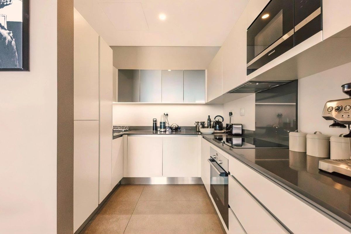 Modern galley-style kitchen featuring sleek handleless cabinetry, stone countertops, integrated oven, electric cooktop, and built-in microwave.
