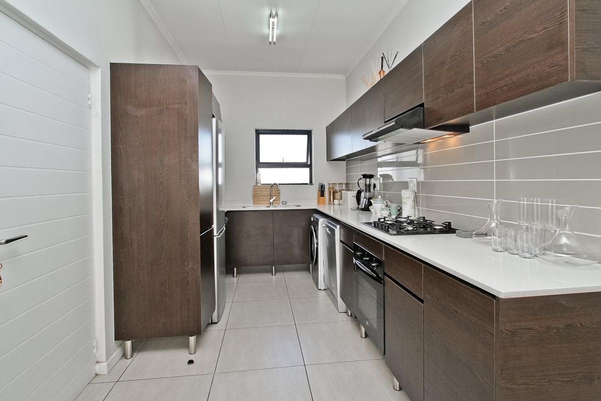 Modern galley-style kitchen featuring dark wood cabinetry, white stone countertops, gas hob, built-in oven, and sleek tiled finishes.