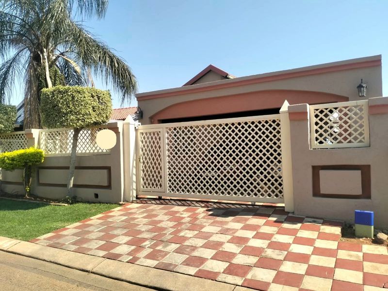 Front view of the property featuring a secure lattice gate, perimeter wall, and a checkered paved driveway.