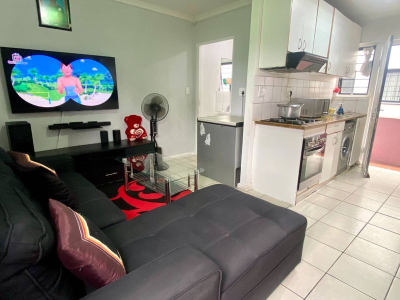Open-plan living area featuring a compact kitchen with built-in cabinetry, oven, and hob, seamlessly connected to the lounge space with tiled flooring throughout.