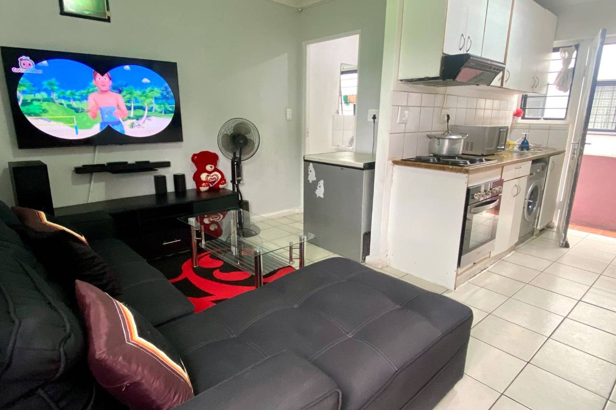 Open-plan living area featuring a compact kitchen with built-in cabinetry, oven, and hob, seamlessly connected to the lounge space with tiled flooring throughout.