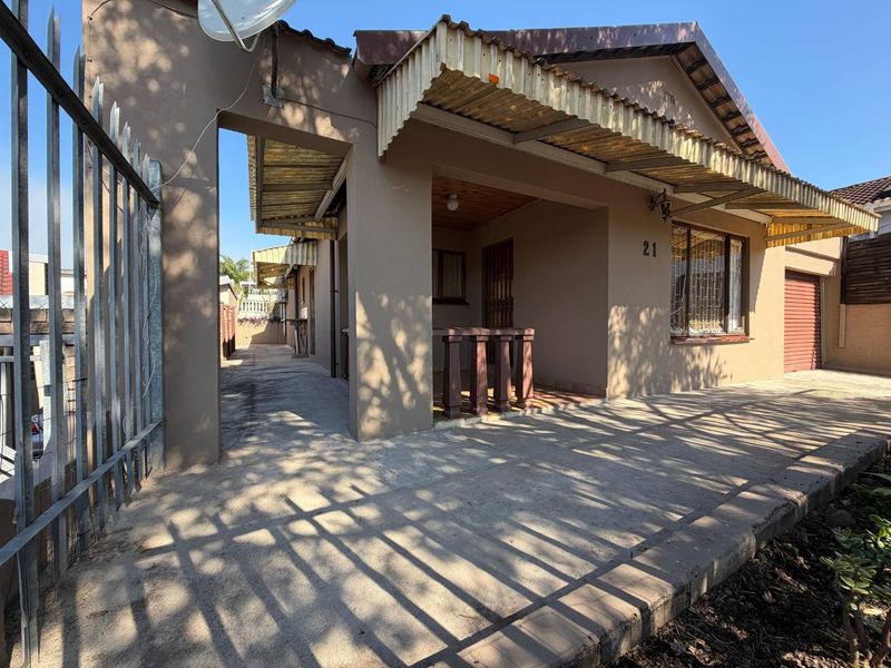 Front exterior view of the property featuring a covered entrance area, concrete driveway, and security fencing.
