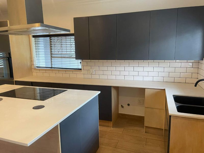 Modern kitchen featuring dark cabinetry, stone countertops, subway tile backsplash, a central island with a built-in hob, and integrated oven.
