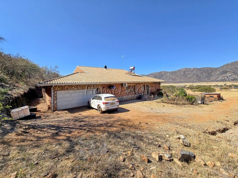 Front exterior view of a small holding property featuring stone cladding, a tiled roof, and a garage, set against a rural landscape.