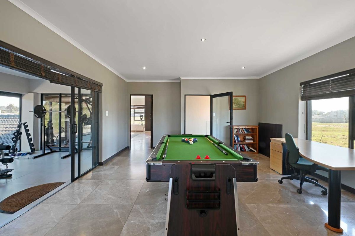 A spacious multi-purpose living area featuring large format floor tiles, recessed lighting, and sliding glass doors providing access to an adjacent gym space.