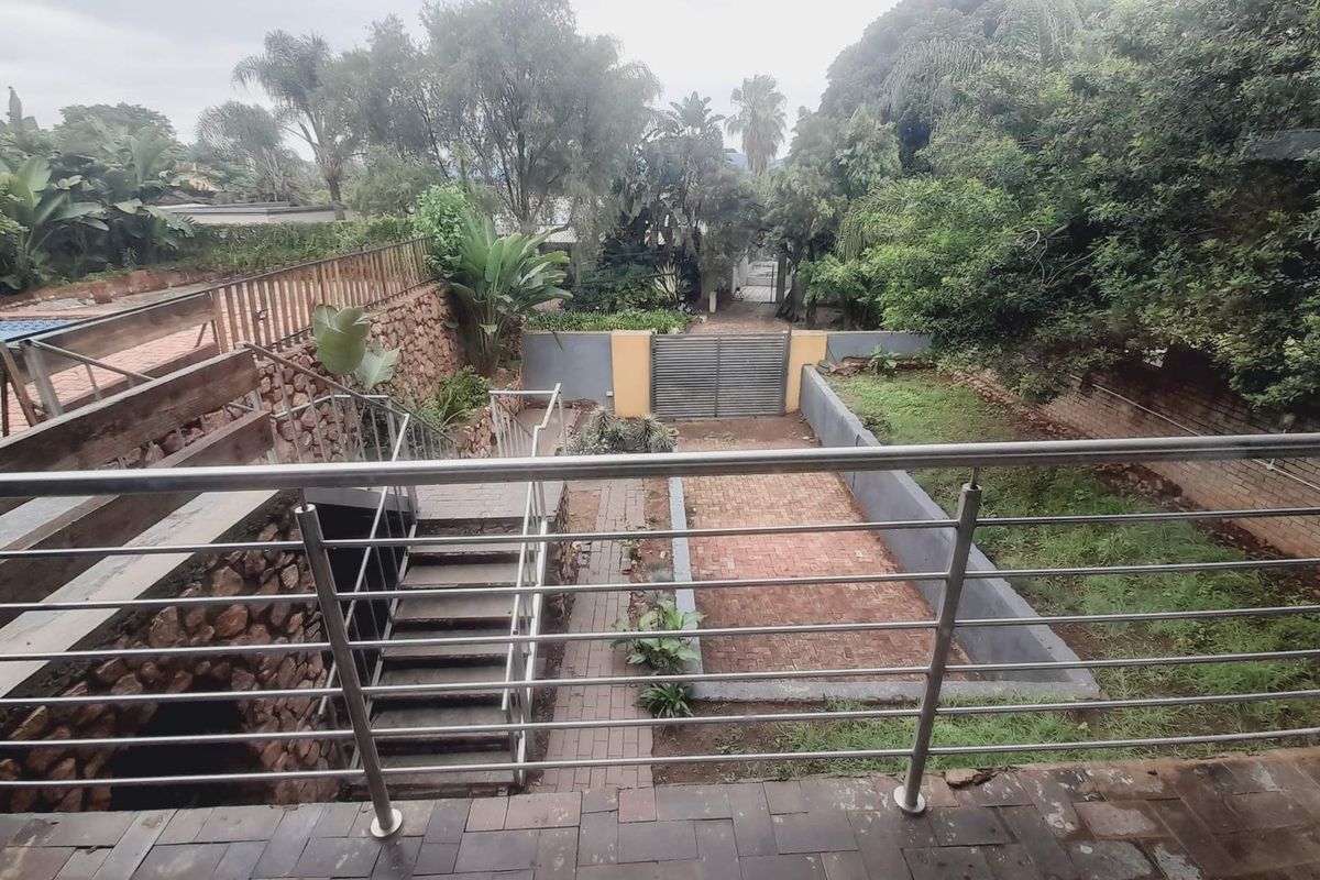 An elevated view of the rear garden featuring a paved patio area, stone retaining walls, a swimming pool, and a gated entrance.