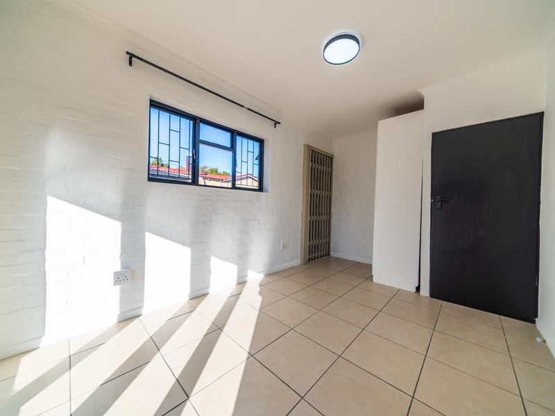A bright, empty bedroom featuring tiled flooring, painted brick walls, and security features on the window and door.
