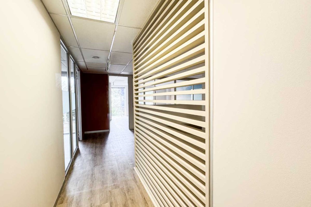 A bright, modern office hallway featuring a decorative slatted timber partition, suspended ceiling with recessed lighting, and durable laminate flooring.