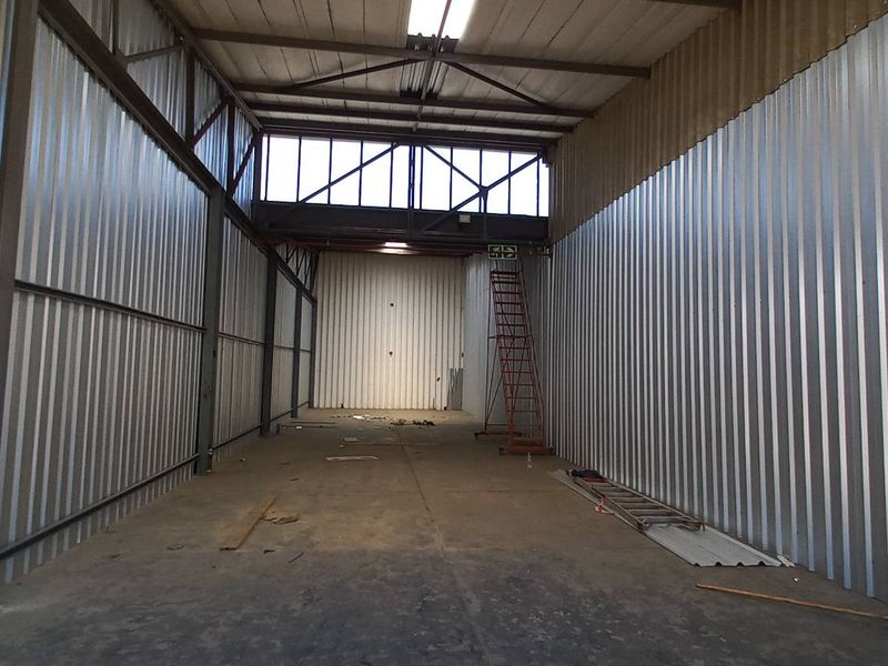 Spacious industrial utility area featuring corrugated metal walls, exposed steel roof trusses, and concrete flooring, suitable for storage or workshop use.