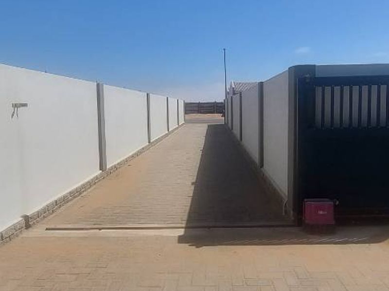 A paved driveway leading to a secure entrance, featuring high boundary walls and a sliding gate.
