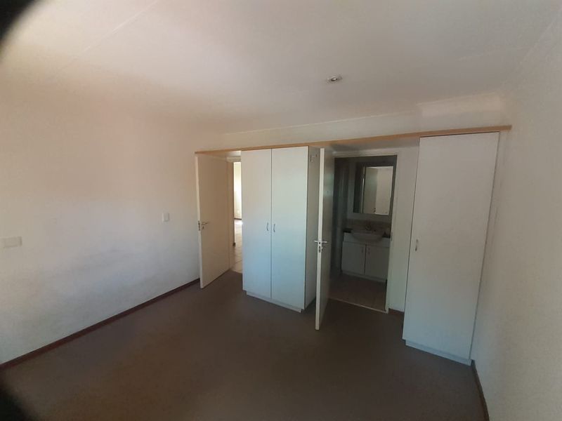 An empty bedroom featuring built-in cupboards and direct access to an en-suite bathroom, requiring minor cosmetic updates to improve its overall appeal.
