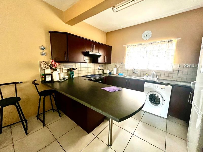 Functional kitchen featuring dark wood cabinetry, a breakfast bar, tiled backsplash, and integrated appliances with a practical layout.
