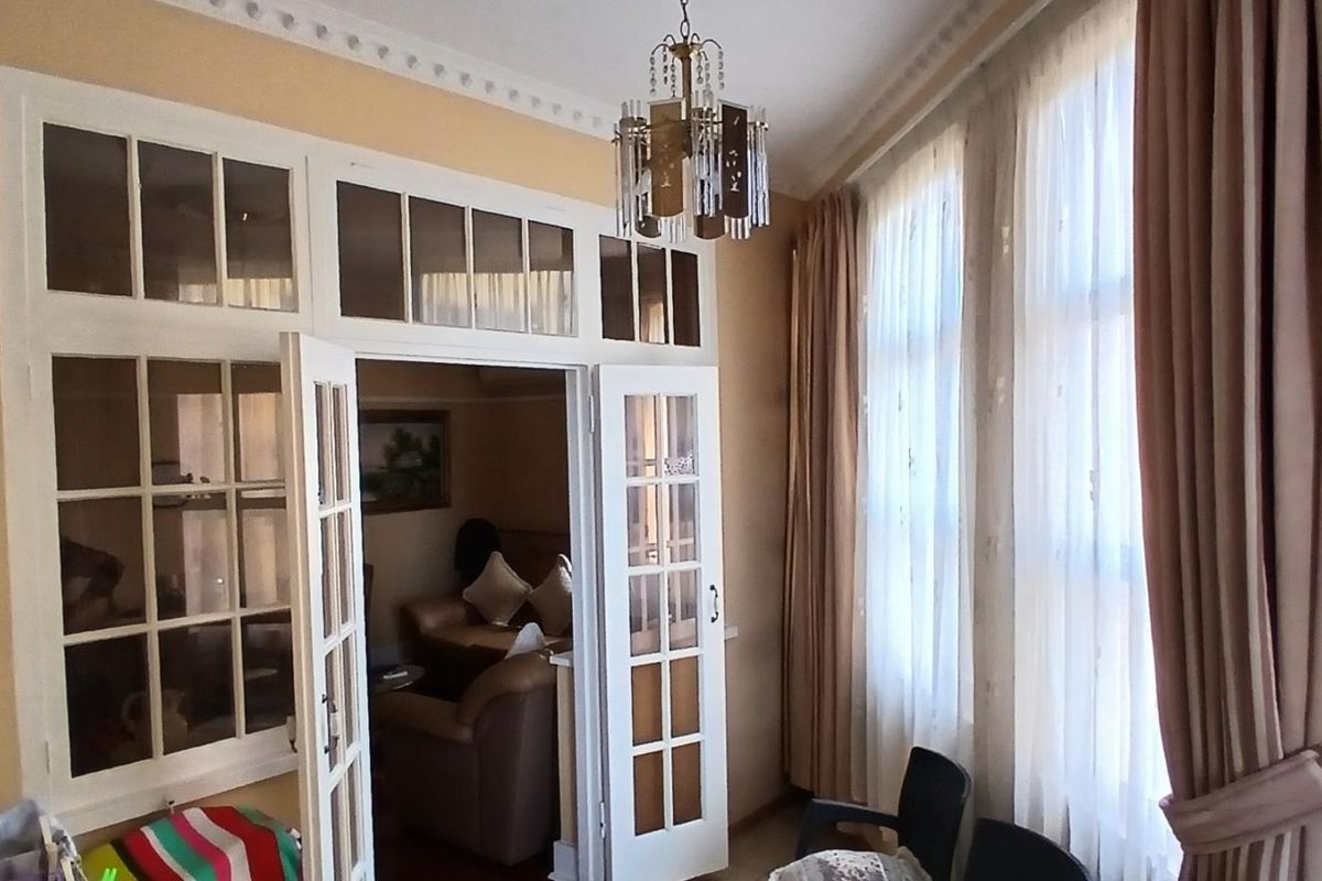 A living room featuring classic french doors with transom windows, decorative crown molding, and a central chandelier, offering a traditional aesthetic.