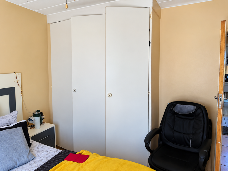 A bedroom featuring a built-in white wardrobe with three doors and a textured tongue and groove ceiling.