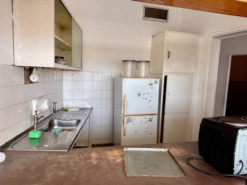 A dated kitchen featuring a stainless steel sink, tiled backsplash, and built-in cabinetry, offering significant potential for modernization and renovation.