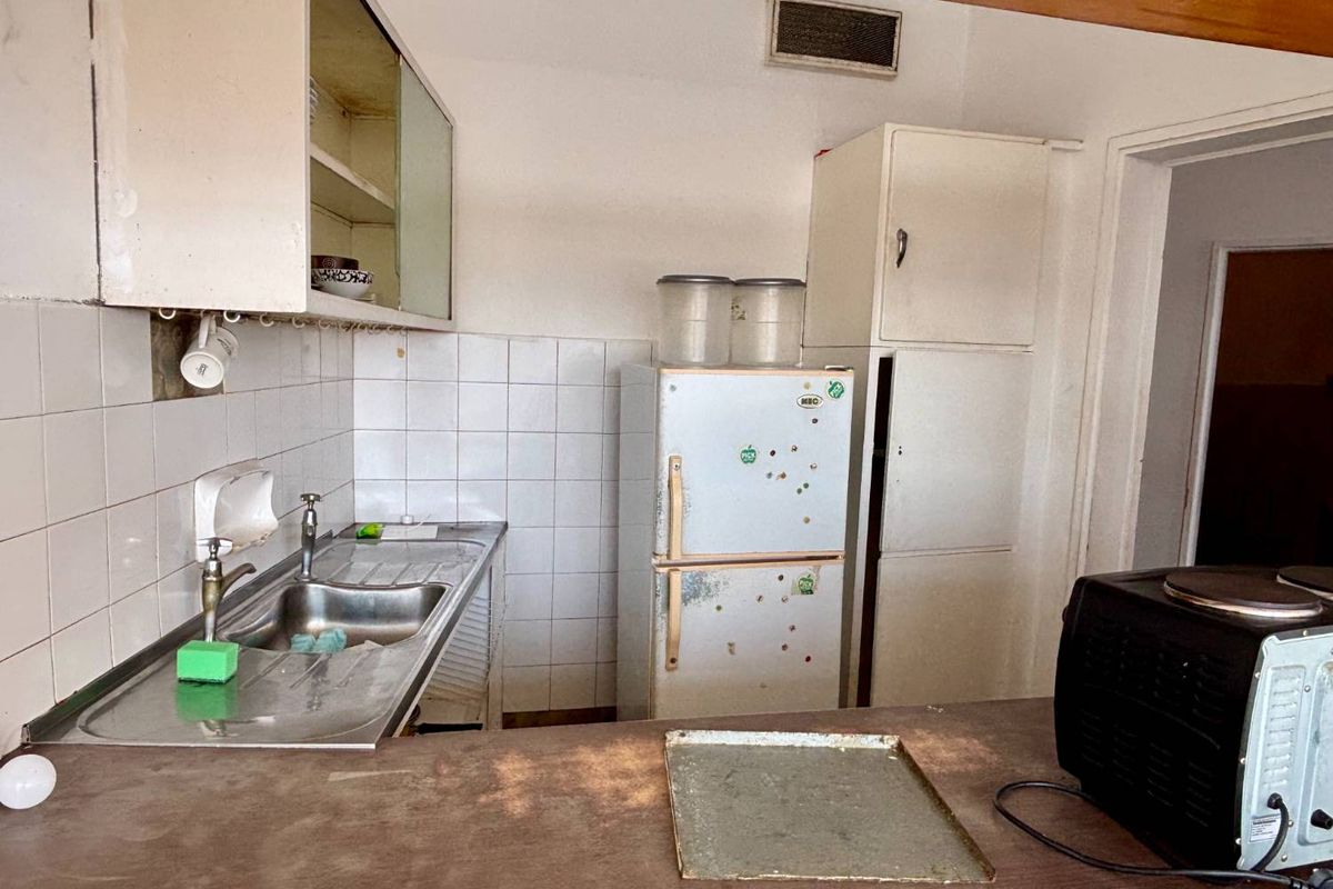 A dated kitchen featuring a stainless steel sink, tiled backsplash, and built-in cabinetry, offering significant potential for modernization and renovation.