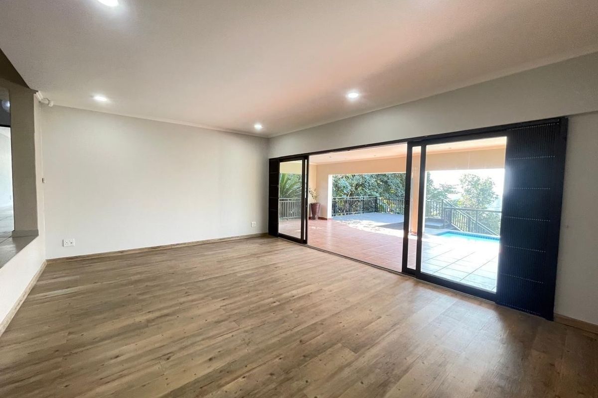 Spacious, light-filled living area featuring modern laminate flooring, recessed lighting, and large sliding glass doors opening onto a covered patio and pool area.