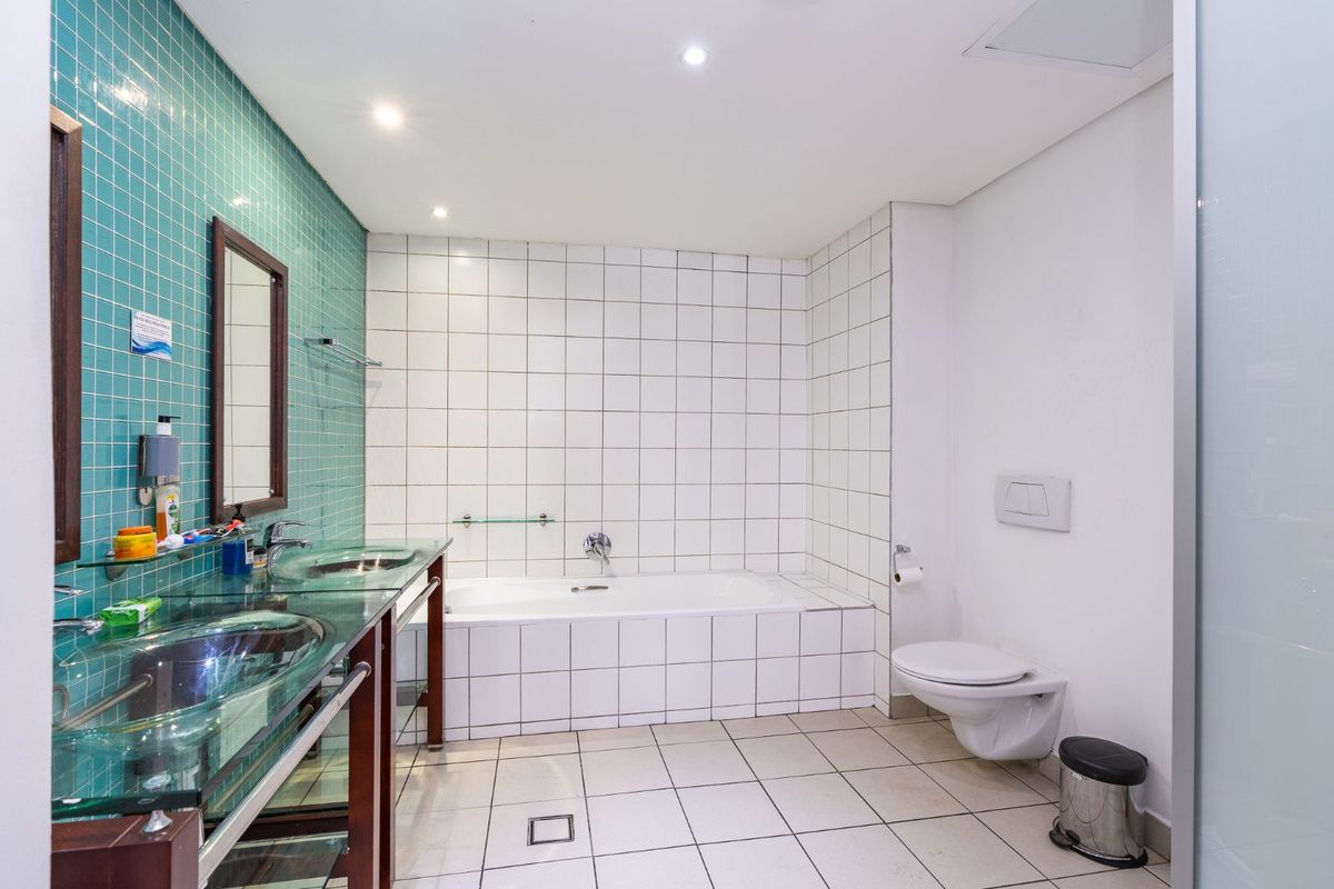 Modern bathroom featuring a double vanity with glass vessel sinks, a built-in bathtub, and a wall-mounted toilet with contemporary tiled finishes.