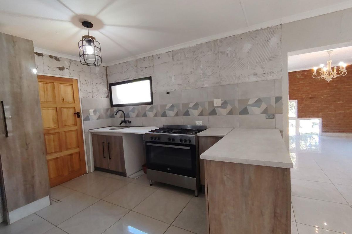 Kitchen area featuring wood-look cabinetry, a freestanding gas stove, and tiled flooring, currently requiring completion of wall finishes and tiling.