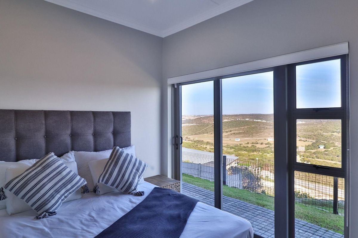A bright bedroom featuring large sliding glass doors that open to a paved patio area with expansive landscape views.