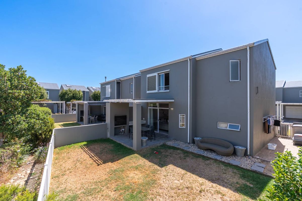 Rear view of the apartment featuring a covered patio with a built-in braai, sliding door access, and a private fenced garden area.