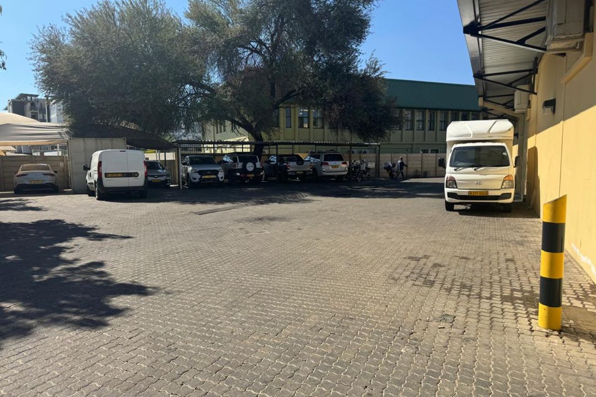 Industrial property exterior featuring a paved parking area with covered parking bays and adjacent building structure.