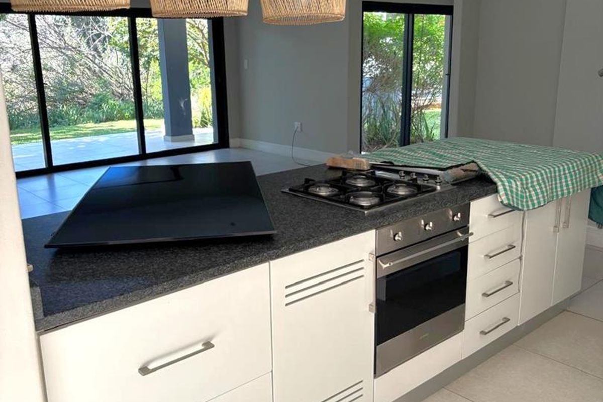 Modern kitchen island featuring granite countertops, a built-in gas hob, and oven, overlooking a bright living area with large sliding glass doors.