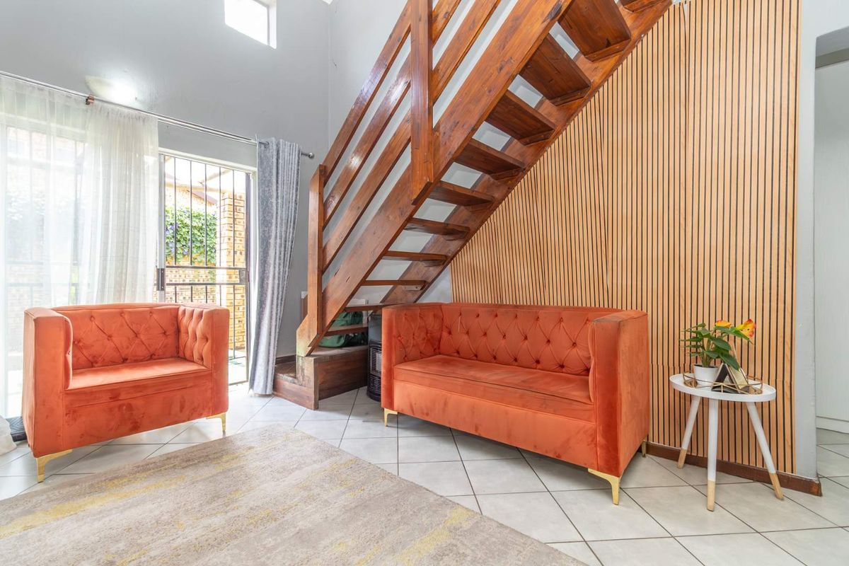 Living area featuring a wooden staircase, decorative slatted timber wall paneling, and tiled flooring with access to an outdoor patio through a sliding door.