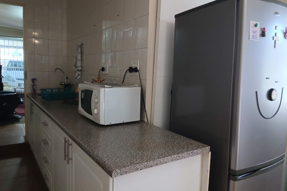 A functional kitchen area featuring white cabinetry, tiled splashbacks, and a laminate countertop with integrated sink and power points.