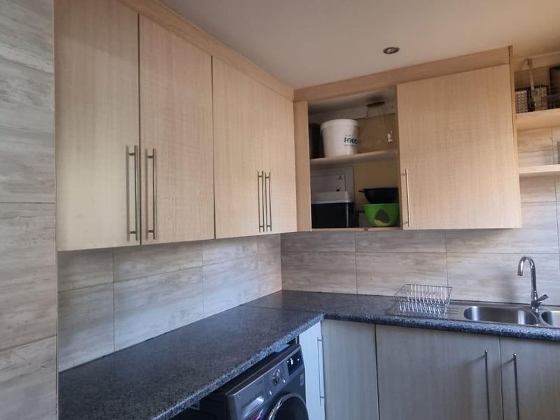 A functional kitchen featuring light wood-look cabinetry, dark granite countertops, a stainless steel sink, and modern tiled backsplash with recessed lighting.