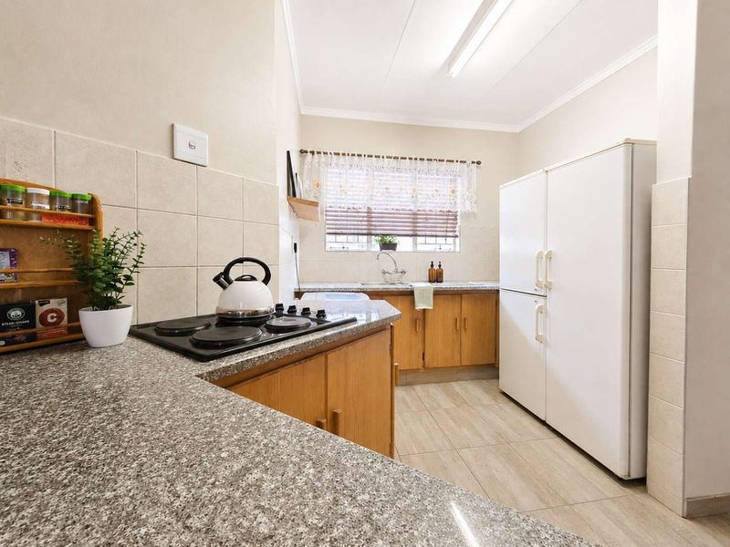 A functional kitchen featuring wooden cabinetry, granite countertops, an electric hob, and tiled finishes, offering a practical layout for daily meal preparation.