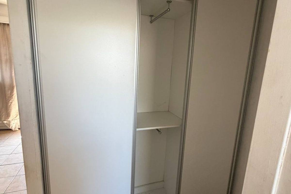 A bedroom featuring a built-in sliding door wardrobe with internal shelving and hanging rail, complemented by neutral tiled flooring.