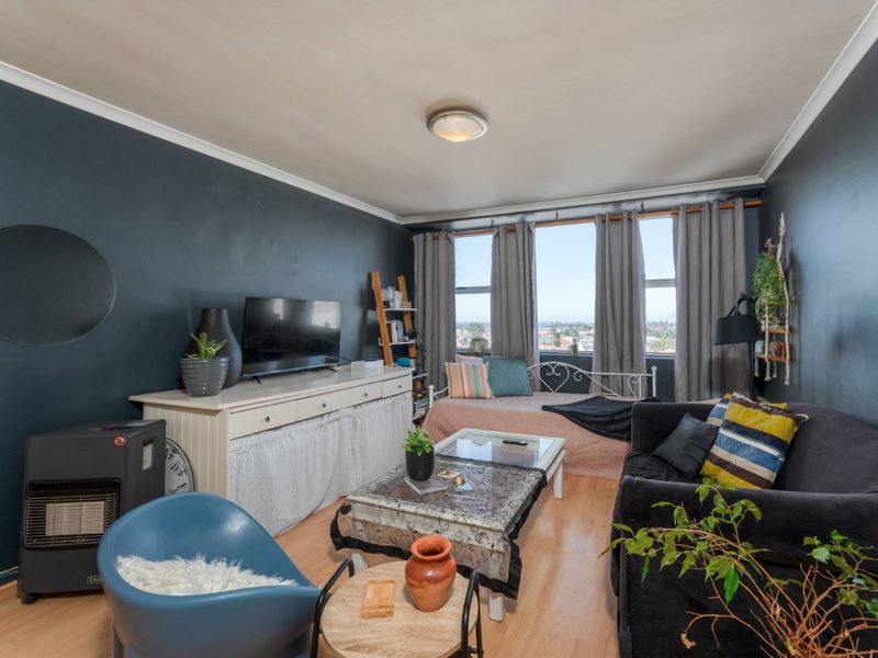 A living room featuring laminate flooring, dark accent walls, and large windows providing natural light and an elevated urban view.