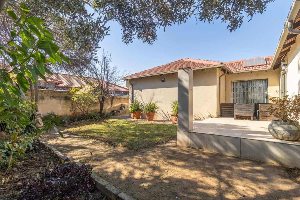 Rear exterior view featuring a tiled patio, sliding glass doors, solar panel, and a garden area with perimeter walling.
