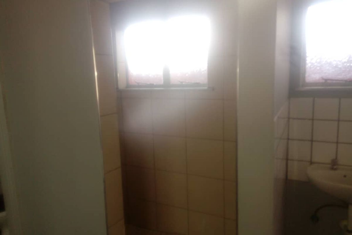 A functional bathroom space featuring tiled shower enclosure and a wall-mounted basin, requiring cosmetic updates to improve the overall aesthetic.