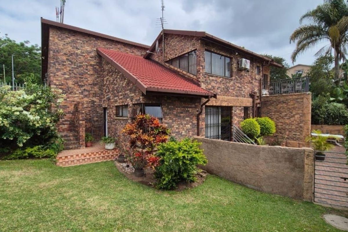 Rear view of a multi-level face brick house featuring a tiled roof, security gates, and a landscaped garden area.