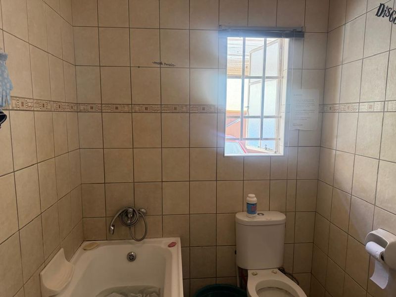 A compact bathroom featuring full-height ceramic wall tiling, a built-in bathtub with chrome mixer, and a standard toilet.