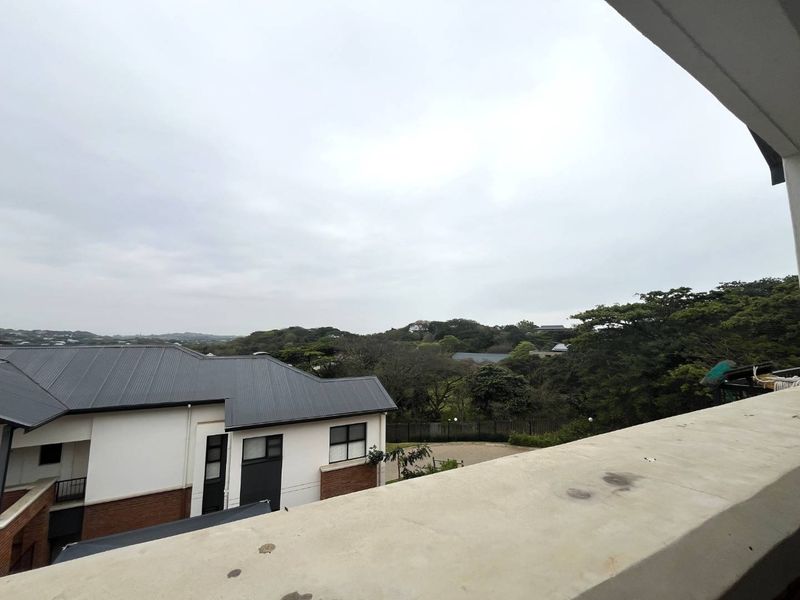 Elevated view from a balcony overlooking surrounding residential buildings and lush green landscape under an overcast sky.