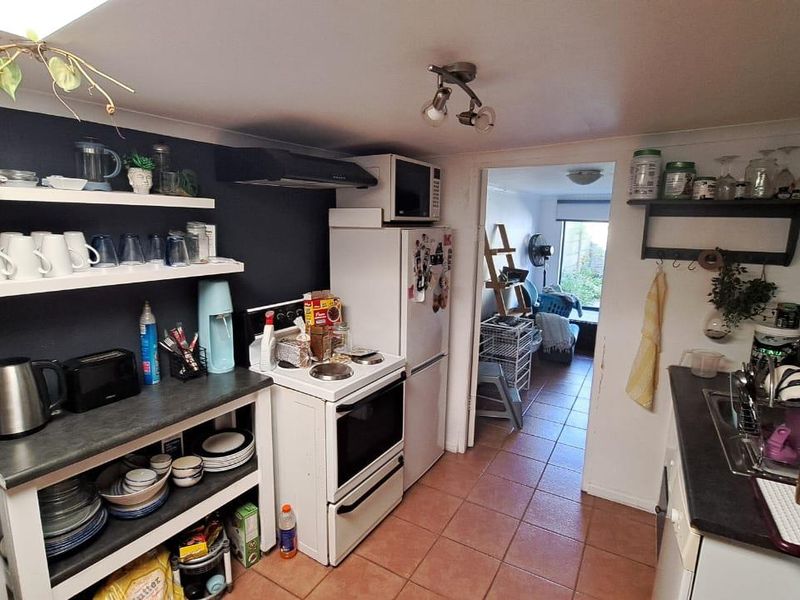 Compact kitchen featuring open shelving, electric stove with extractor fan, tiled flooring, and laminate countertops, leading through to an adjacent living area.