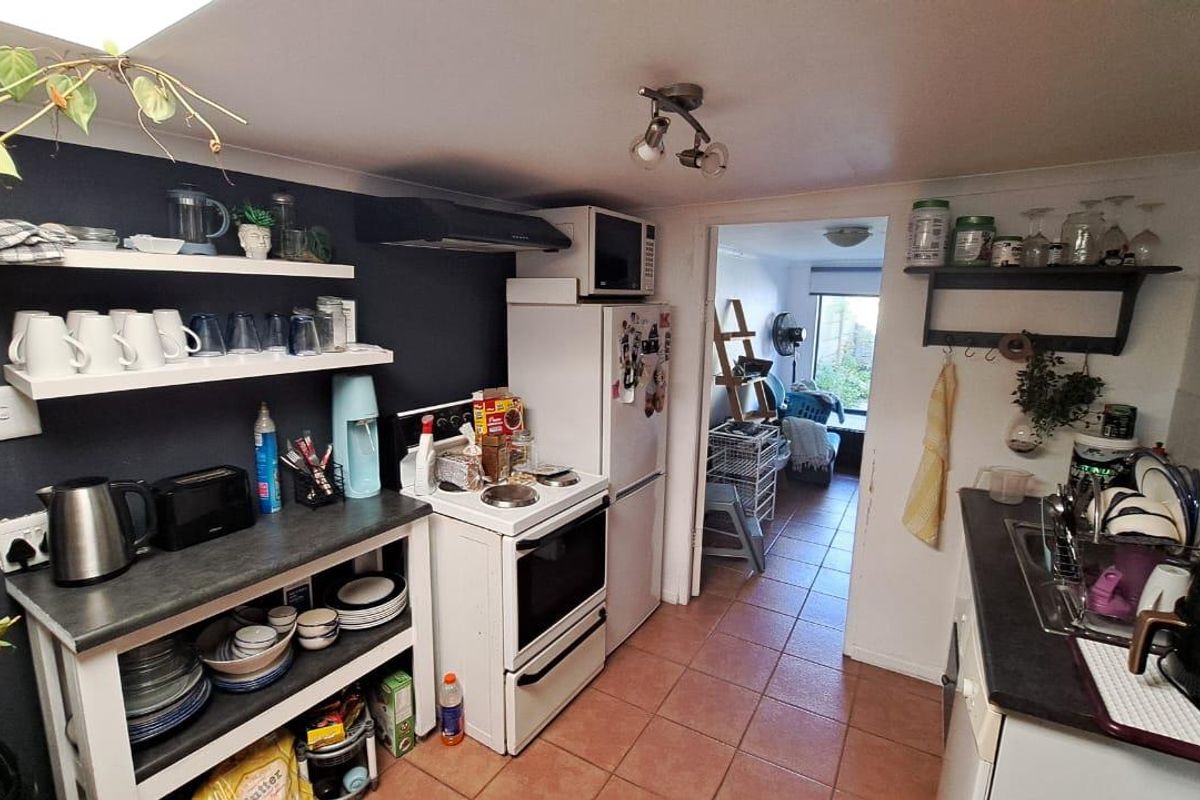 Compact kitchen featuring open shelving, electric stove with extractor fan, tiled flooring, and laminate countertops, leading through to an adjacent living area.
