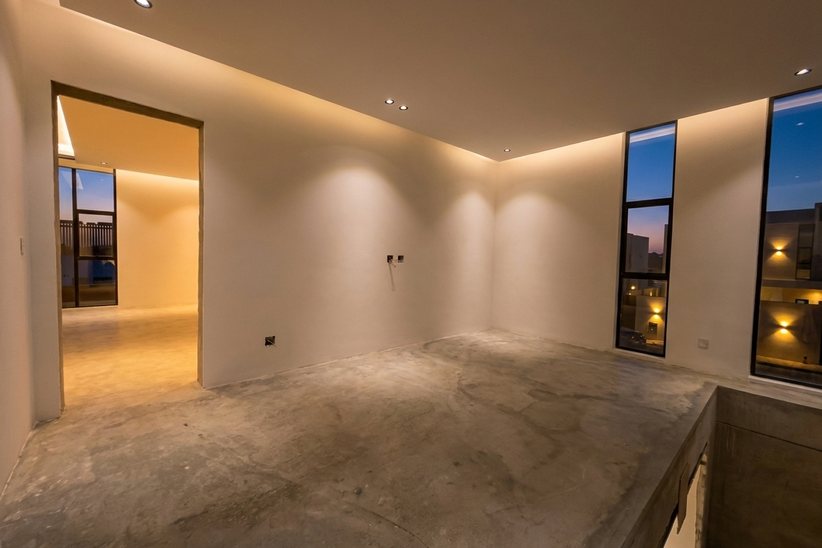 A spacious, modern interior room featuring polished concrete floors, recessed ceiling lighting, and tall floor-to-ceiling windows with views of the surrounding neighborhood.