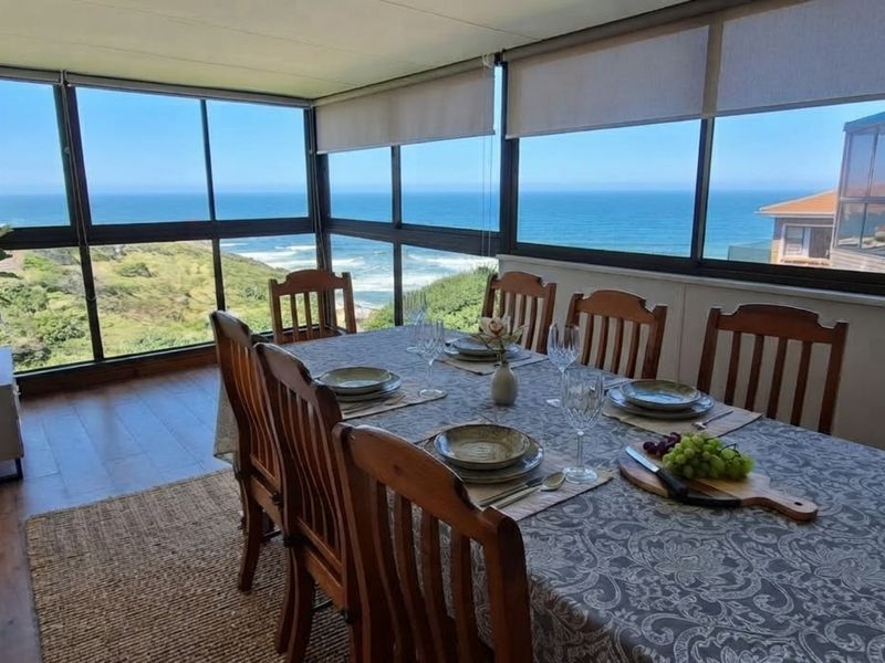 Enclosed patio or sunroom featuring expansive ocean views, large glass windows, and laminate flooring, perfect for dining while enjoying the coastal scenery.