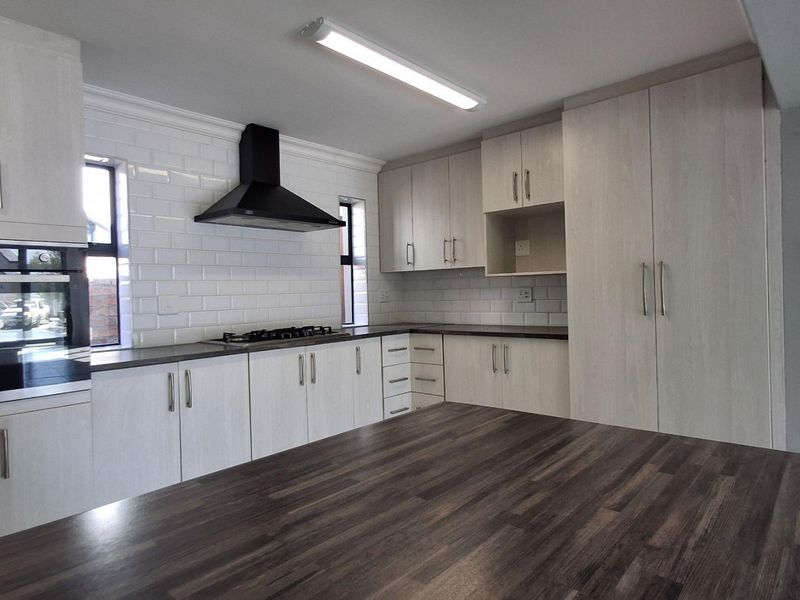 Modern kitchen featuring light wood-grain cabinetry, subway tile backsplash, dark laminate countertops, and integrated appliances including a gas hob and oven.