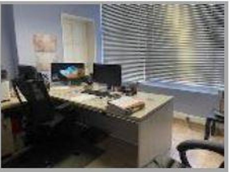 A functional office space featuring laminate flooring and adjustable venetian blinds, providing a practical work environment.