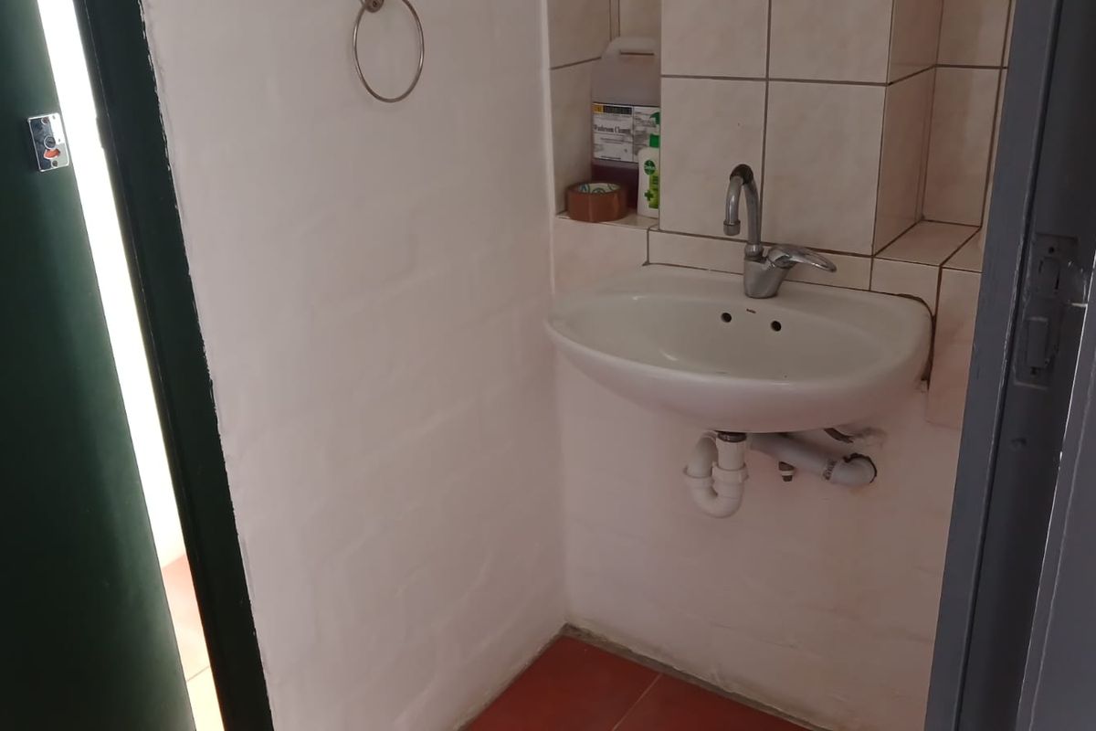 A small, functional office washroom featuring a wall-mounted basin, tiled splashback, and basic plumbing fixtures.